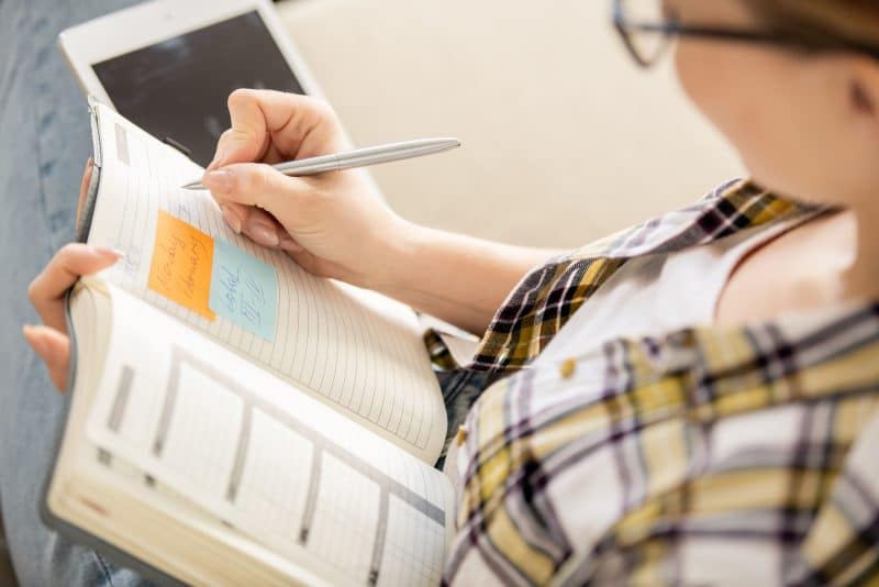 Close-up of young woman making notes in diary while setting goals